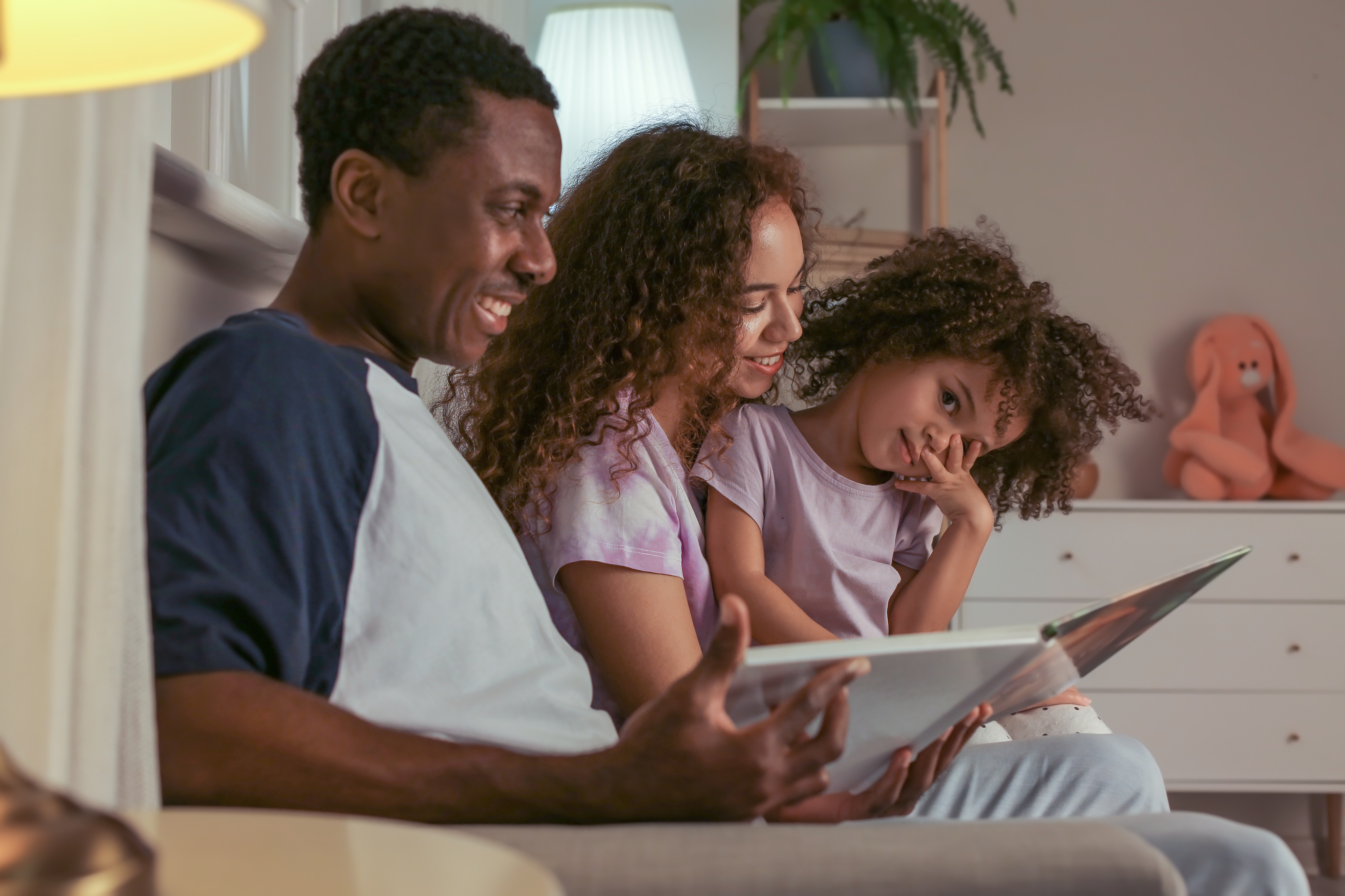 Image of a mother and father reading a book with their daughter